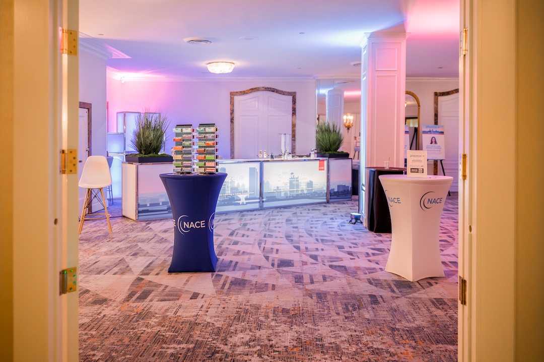 pink and blue lit room with lit up registration desk in background and two tall tables in foreground