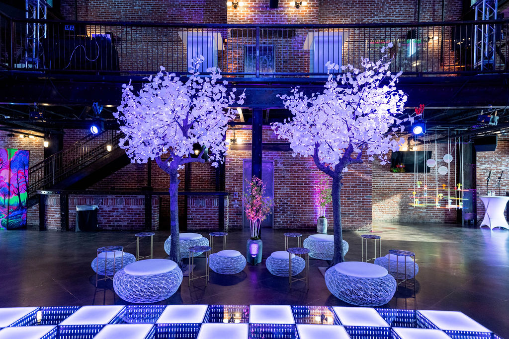 white neon lit trees, ottoman stools, and dance floor in industrial building